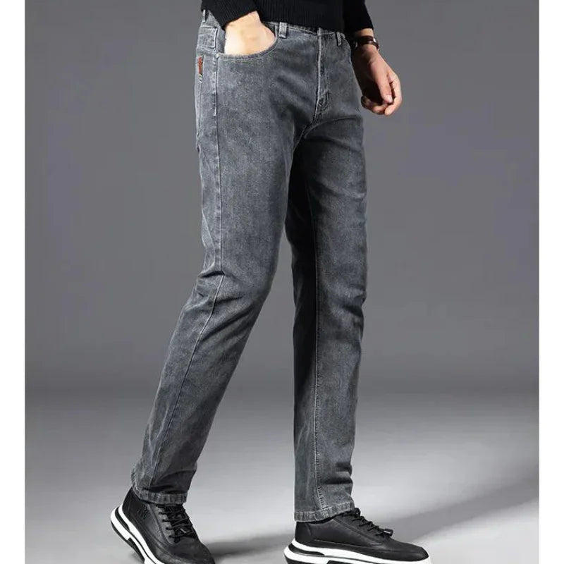 A person stands against a plain gray background, wearing heavyweight denim straight-leg jeans, a black long-sleeve shirt, and black sneakers with white soles. The persons head is not visible in the image.