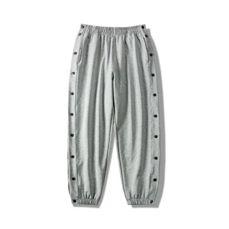 Light gray button-up gym pants with an elastic waistband and cuffs, featuring snap buttons down the sides of both legs and crafted from moisture wicking fabric for ultimate comfort.