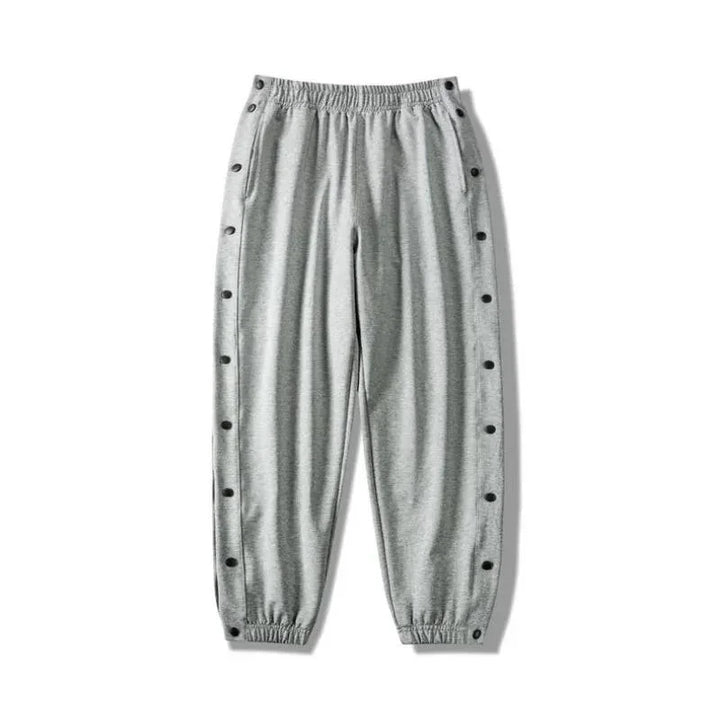 Light gray button-up gym pants with an elastic waistband and cuffs, featuring snap buttons down the sides of both legs and crafted from moisture wicking fabric for ultimate comfort.