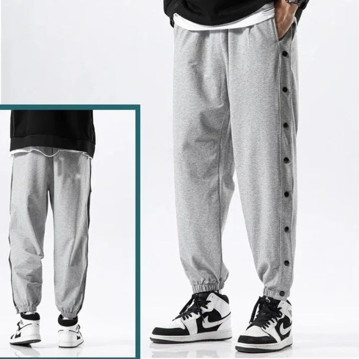 A person wearing grey button-up gym pants with black snap buttons down the sides, paired with white and black sneakers. An inset shows a rear view of the pants, made from moisture wicking fabric, and sneakers.