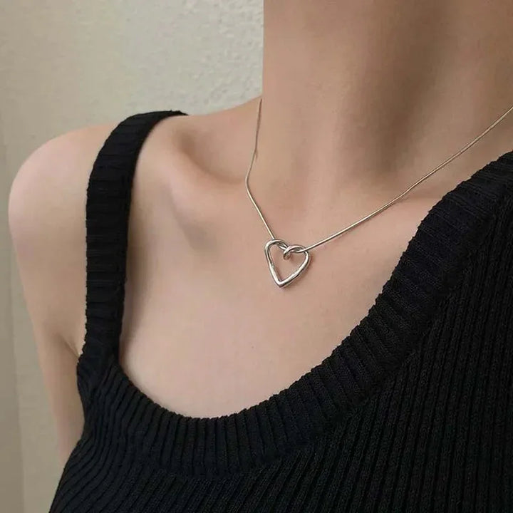 Woman wearing a silver heart pendant necklace with a black ribbed top, Rovelli jewelry