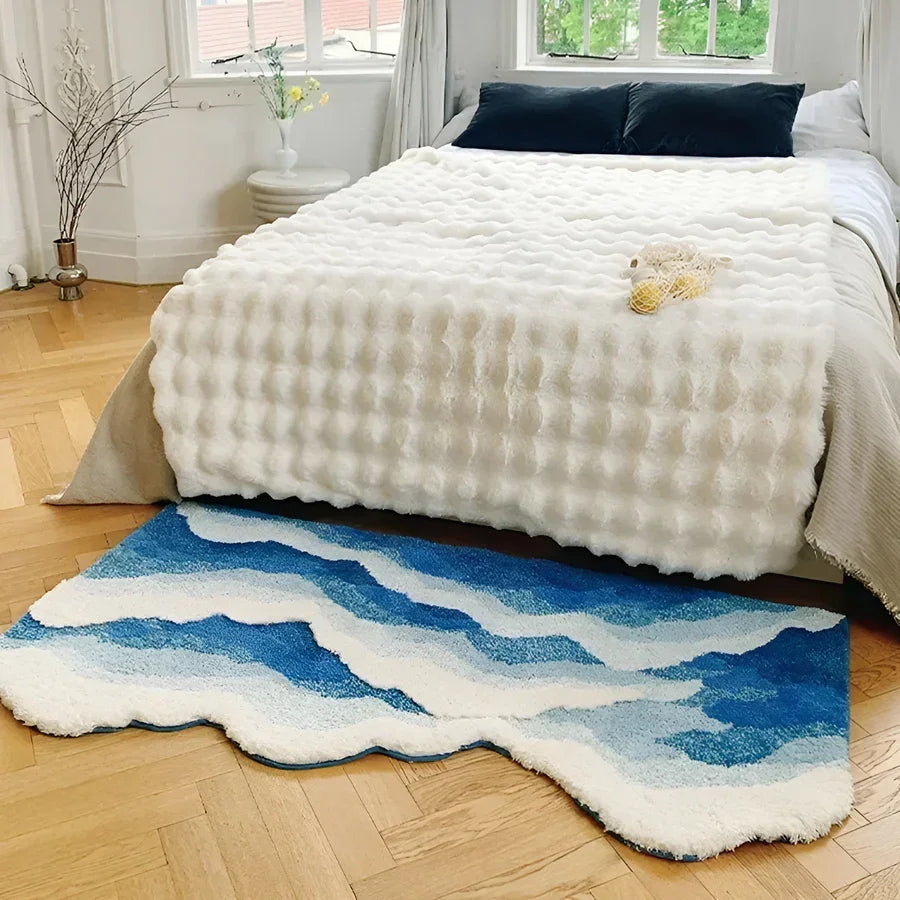 Modern bedroom with textured white bedspread, blue wave rug, and natural sunlight, Rovelli decor.