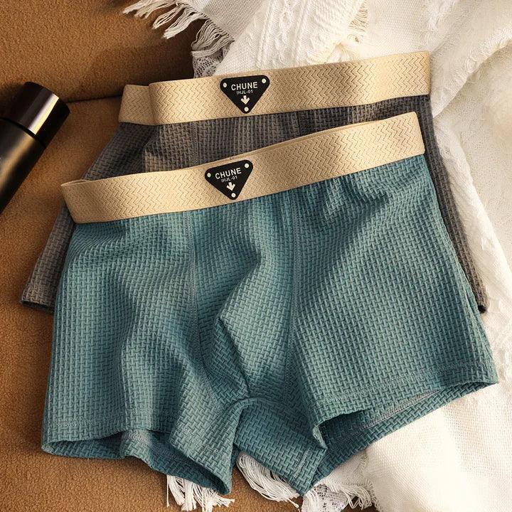 Two pairs of textured men's boxer briefs with beige waistbands on a soft fabric surface