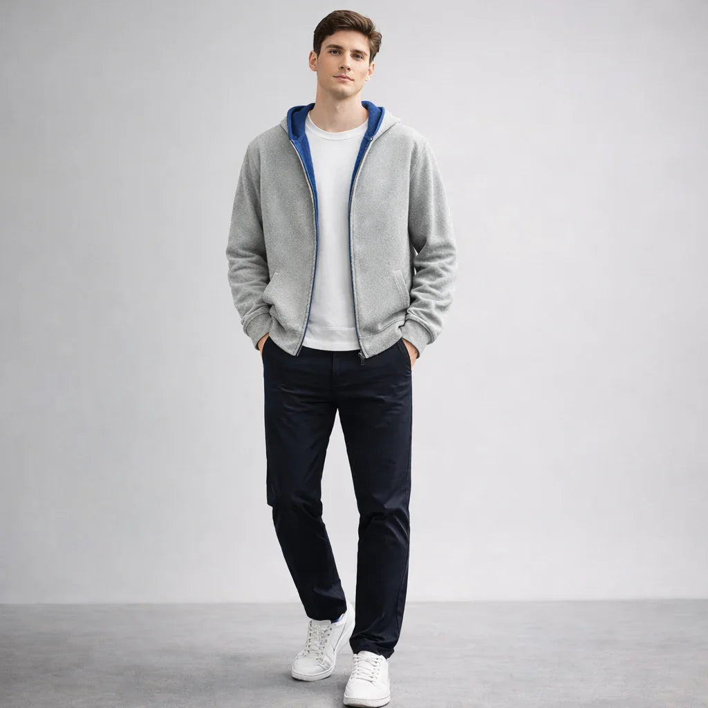 Male model wearing grey zip hoodie, white T-shirt, navy pants, and white sneakers, Rovelli fashion.