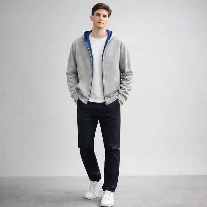Male model wearing grey zip hoodie, white T-shirt, navy pants, and white sneakers, Rovelli fashion.