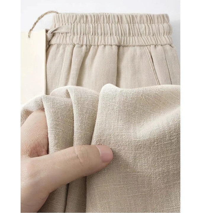Close-up of hand holding beige linen pants with elastic waistband, Rovelli fashion