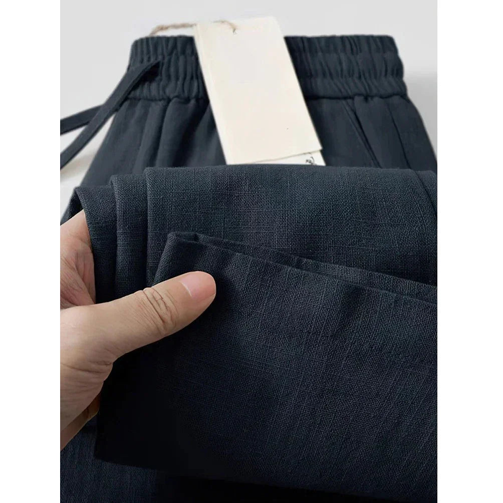 Close-up of hand holding black Rovelli pants with elastic waistband and visible fabric texture