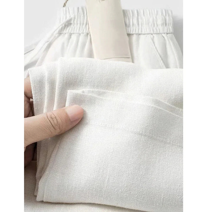 Hand holding soft white linen pants with elastic waistband, Rovelli clothing fabric close-up