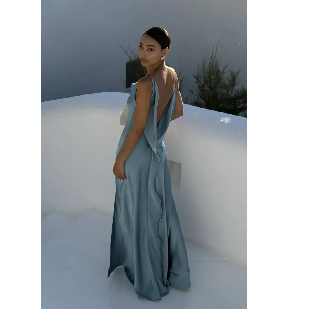 Woman in elegant blue satin backless gown standing on white steps, Rovelli fashion