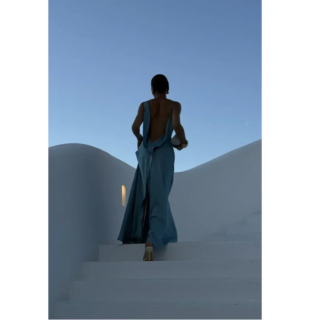 Woman in elegant blue backless dress on white steps at sunset, Rovelli fashion style