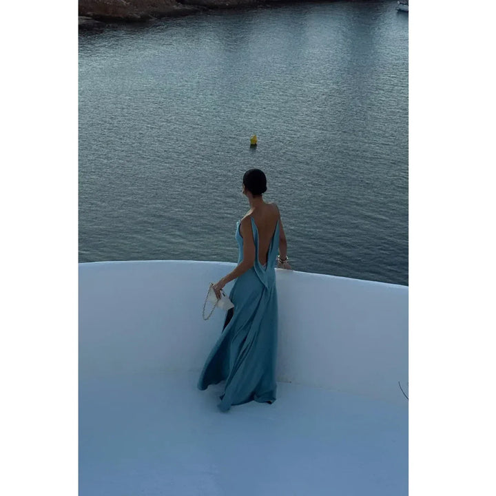 Elegant woman in blue backless dress by waterfront, luxury fashion Rovelli style