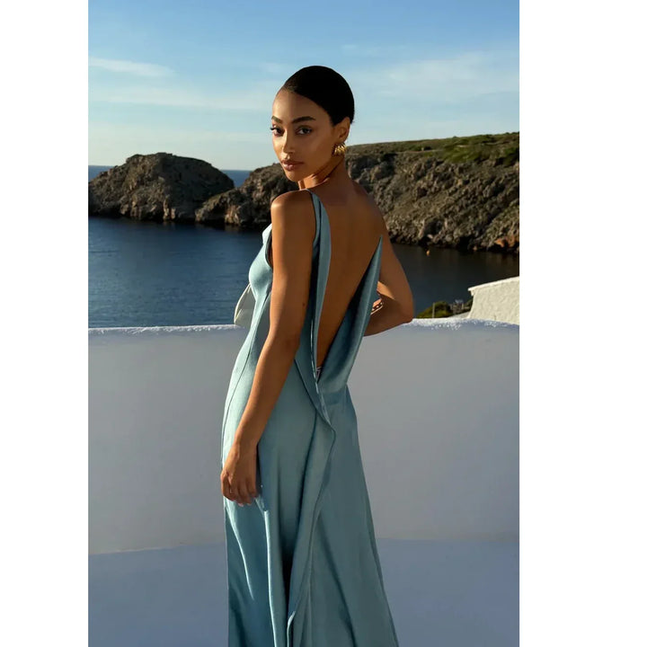 Woman in elegant blue backless dress by the sea, Rovelli fashion, coastal backdrop