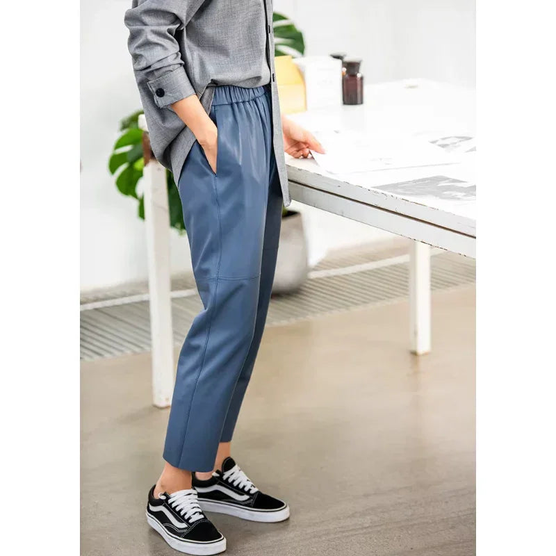 Woman wearing Rovelli light blue leather pants with black sneakers, standing by a white desk