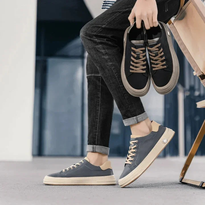Rovelli casual sneakers in grey and beige, worn and held by a person in rolled jeans indoors