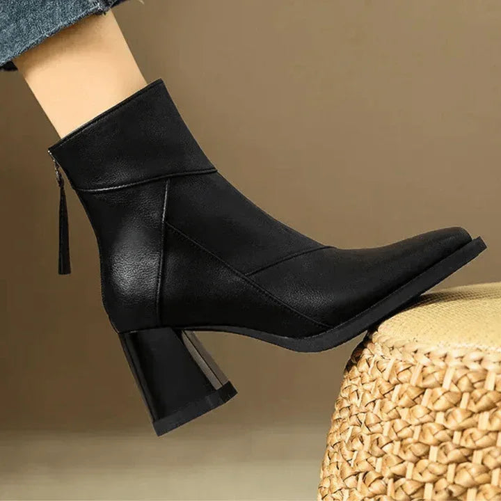 Rovelli black heeled ankle boot with pointed toe and zipper, showcased on woven stool