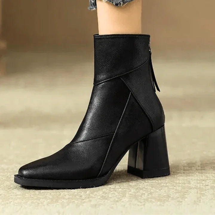 Black leather ankle boot with block heel, side zipper, and pointed toe on beige carpet
