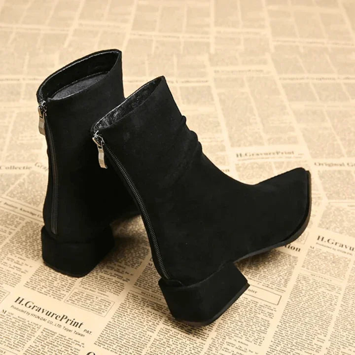 Black suede block heel Valeria boots with side zipper by Rovelli on newspaper background