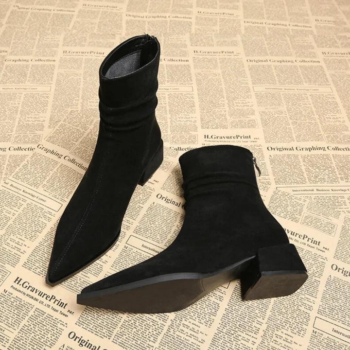 Black suede pointed-toe ankle boots with low block heel on vintage newspaper backdrop, Rovelli