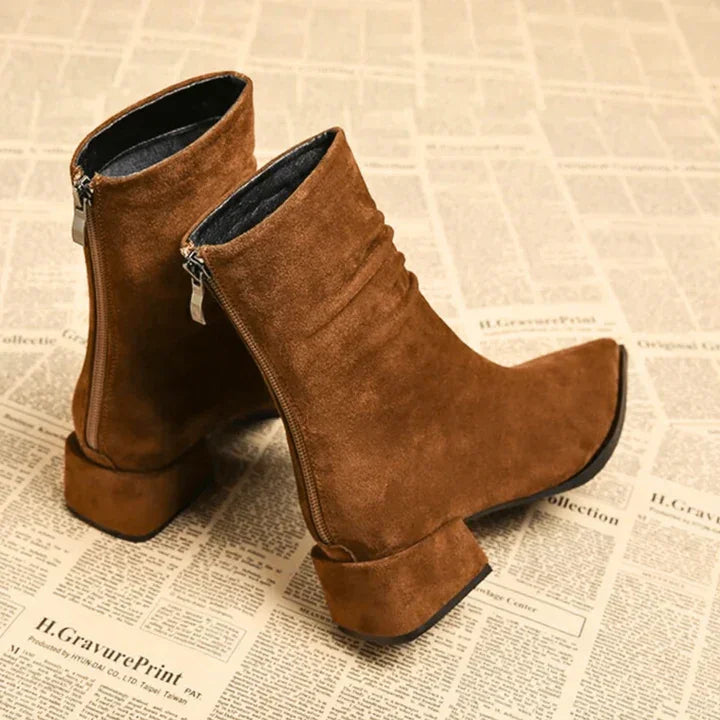 Brown suede ankle boots with block heels, side zippers, on a vintage newspaper background, Rovelli